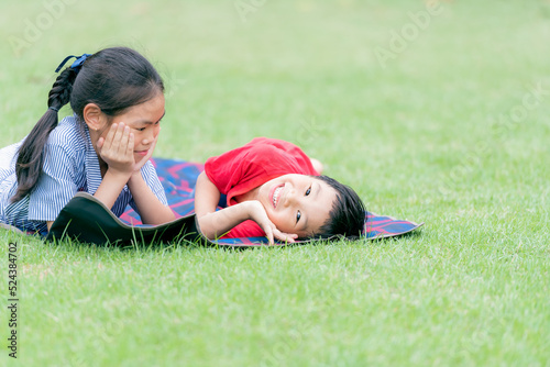 Asian children, 11 year old sisters and 5 year old brothers, are lying on the green field, smiling and enjoying with green nature, to childrens and activity concept.