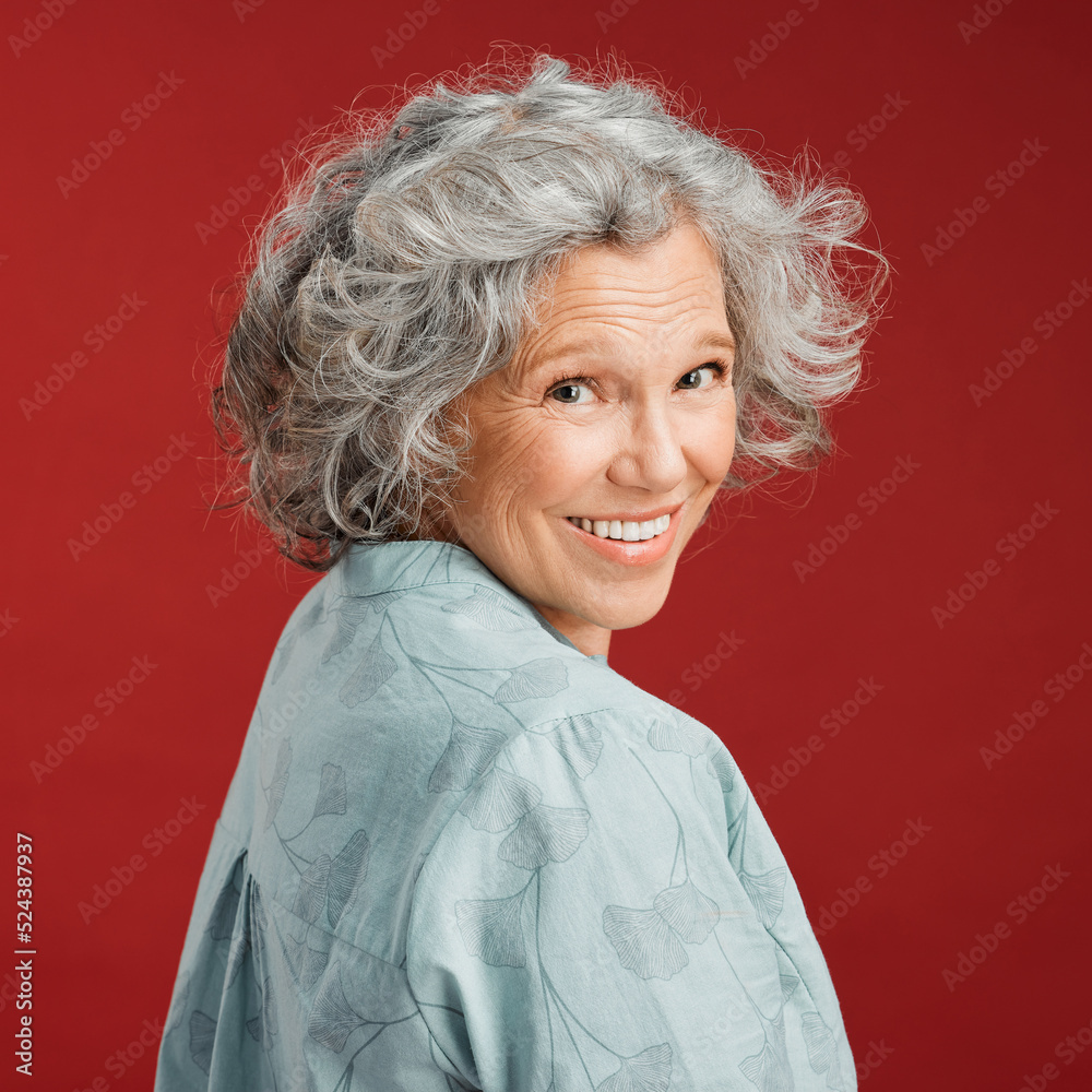.. Confident, happy and smiling senior woman feeling playful and cheerful while posing against red studio background. Portrait of a beautiful, older and retired lady looking back with grey hair.