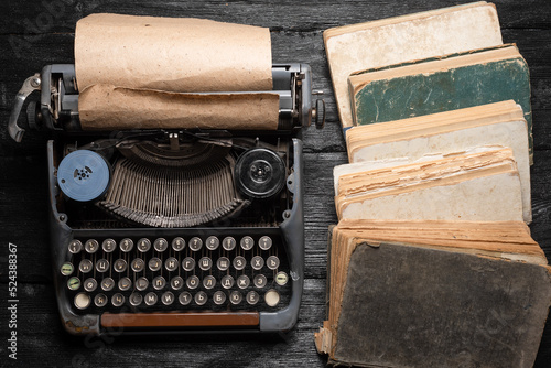 Retro style typewriter and stack of books on the black wooden flat lay background.