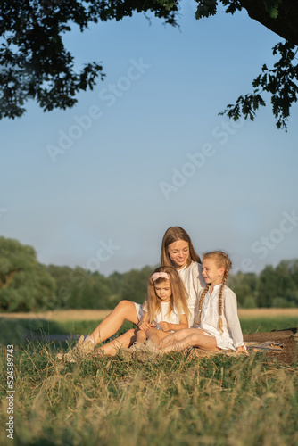 Mother and daughters relax in nature. Vertical photo of a mother with children. Family photo shoot in the village in the field. Psychology of the relationship between mother and child