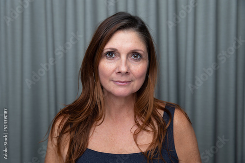 Simple portrait of a beautiful brunette middle aged 40+ 50+ year old woman with long hair looking at the camera making direct eye contact with a neutral expression