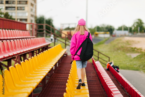 A teenage girl with a backpack walks through the stands of the school stadium. Rear view