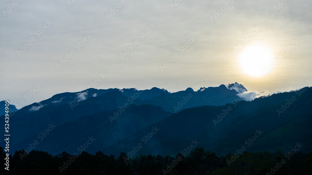 View misty mountains at sunset.  Beautiful view on the mountains from the top through the clouds. Jagged blue silhouettes mountain range. Selective focus.