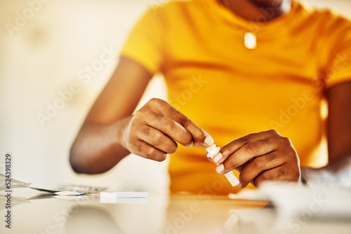 Hands of African female with HIV and Aids at home blood self test kit sitting at a desk waiting to check for results. Closeup of young afro woman with medicine or pills for a medical condition.