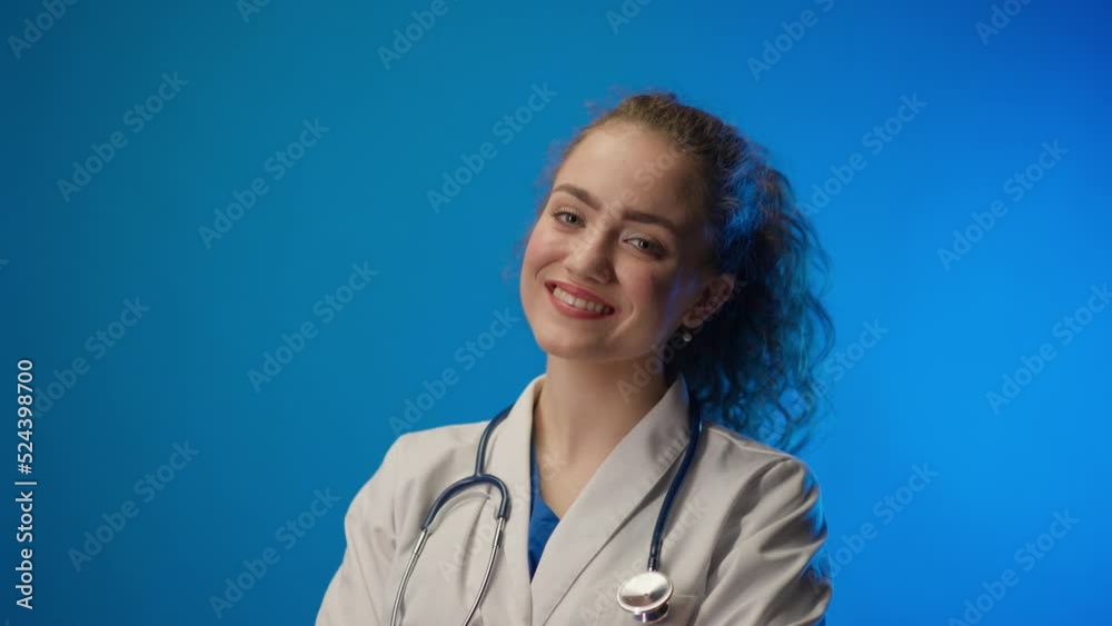 Young female doctor smiling and looking at camera against a blue background. Young female doctor smiling and looking at camera against a blue background.