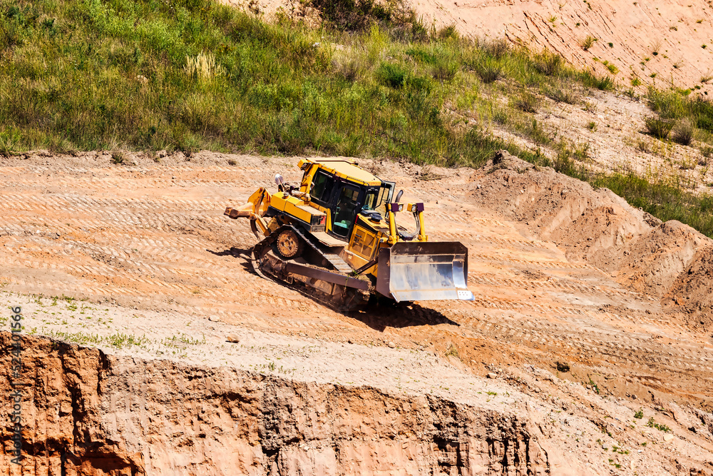A powerful bulldozer in a sand pit is planning a site. Extraction of sand in an open pit. natural building materials. A powerful bulldozer in a sand pit is planning a site. Extraction of sand in an open pit. natural building materials.