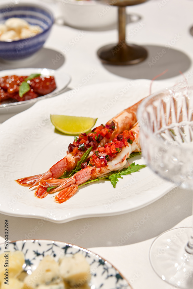 Seafood appetizer - baked langoustines with tomato tartar on white table. Grilled shrimp in italian restaurant menu. Langoustines on white background with shadows. Shrimp appetizer. Baked prawn.