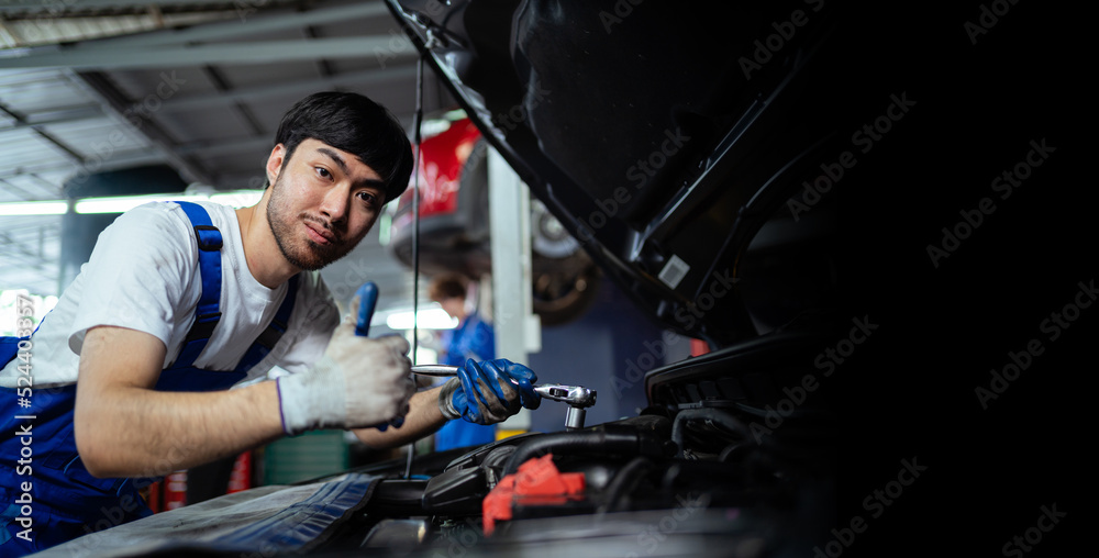 Handsome young Asian mechanic checking his car with a wrench in the service center through the insurance system at the engine repair and inspection center. Handsome young Asian mechanic checking his car with a wrench in the service center through the insurance system at the engine repair and inspection center.