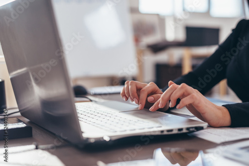 Woman working in an office with a laptop with her hands on the keyboard close-up