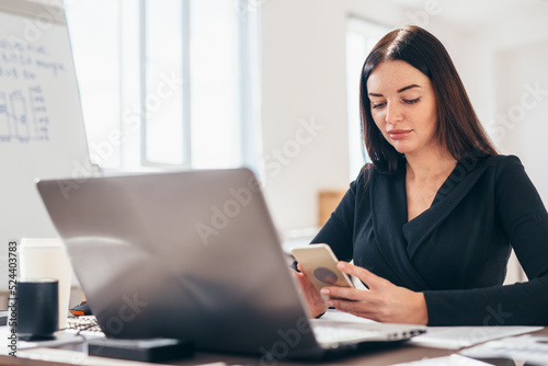 Woman in the office sits at her desk and uses her smartphone.
