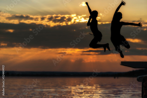 Zwei Kinder springen an einem sch  nen Sommerabend in einen See