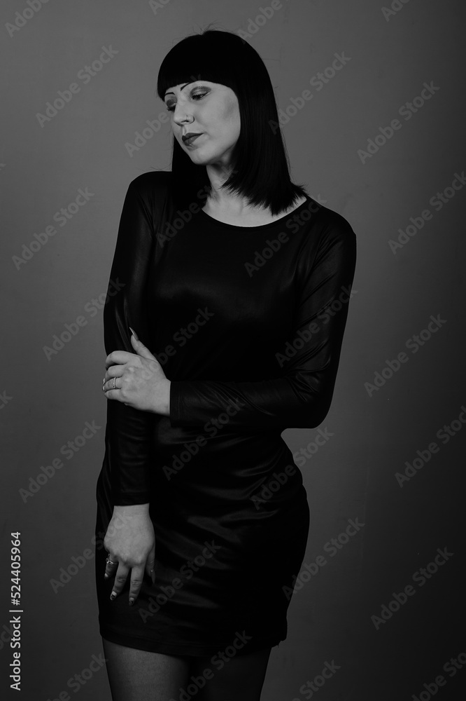 A beautiful girl with dark hair in a black dress poses on a dark background