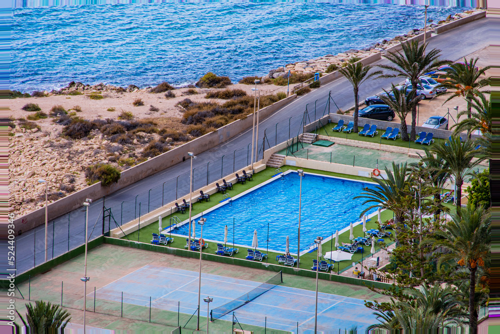  top view of an empty hotel pool with sun loungers on the grass by the seashore