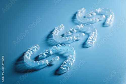 Close up invisible aligners on blue background with copy space. Plastic braces for teeth alignment. Set of three pairs of aligners on a blue background