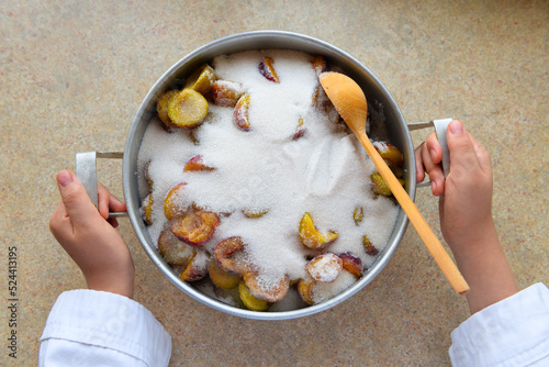 a woman's hand with a saucepan full of plums and sugar for making jam at home, the concept of preserving fruit at home, healthy and delicious food photo