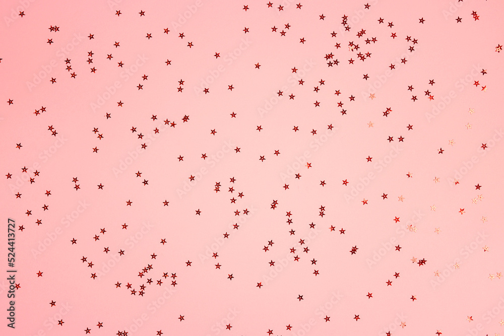 Red star shaped glitter confetti on pink background. Festive flat lay holiday pastel backdrop.