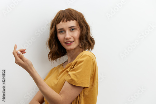 a beautiful, funny, attractive woman in a yellow cotton T-shirt stands on a light background and smiles broadly