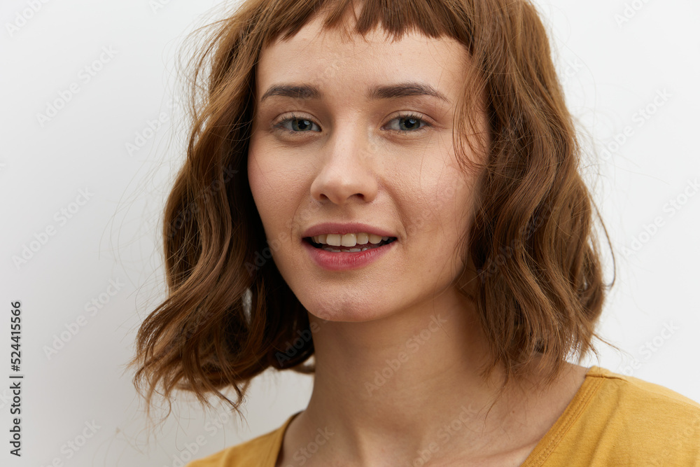 a close, horizontal portrait of a joyful, happy woman in a yellow T-shirt on a light background smiling broadly and looking at the camera a close, horizontal portrait of a joyful, happy woman in a yellow T-shirt on a light background smiling broadly and looking at the camera
