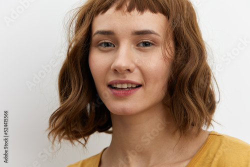 a close, horizontal portrait of a joyful, happy woman in a yellow T-shirt on a light background smiling broadly and looking at the camera