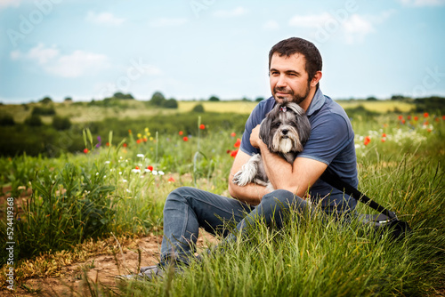 Tranquil and cheerful scene with a white Caucasian bearded man sitting outside in the nature, looking dreamy and hugging his best friend dog.