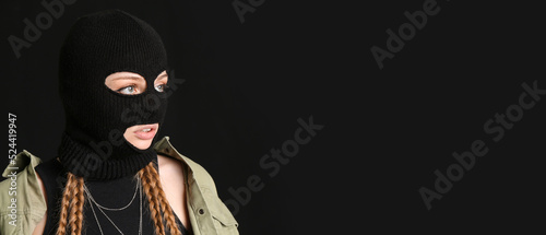 Young woman in balaclava on black background with space for text