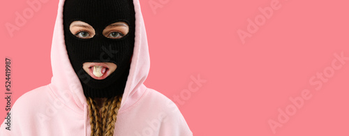 Fotografia Young woman in balaclava and hoodie chewing gum on pink background with space fo