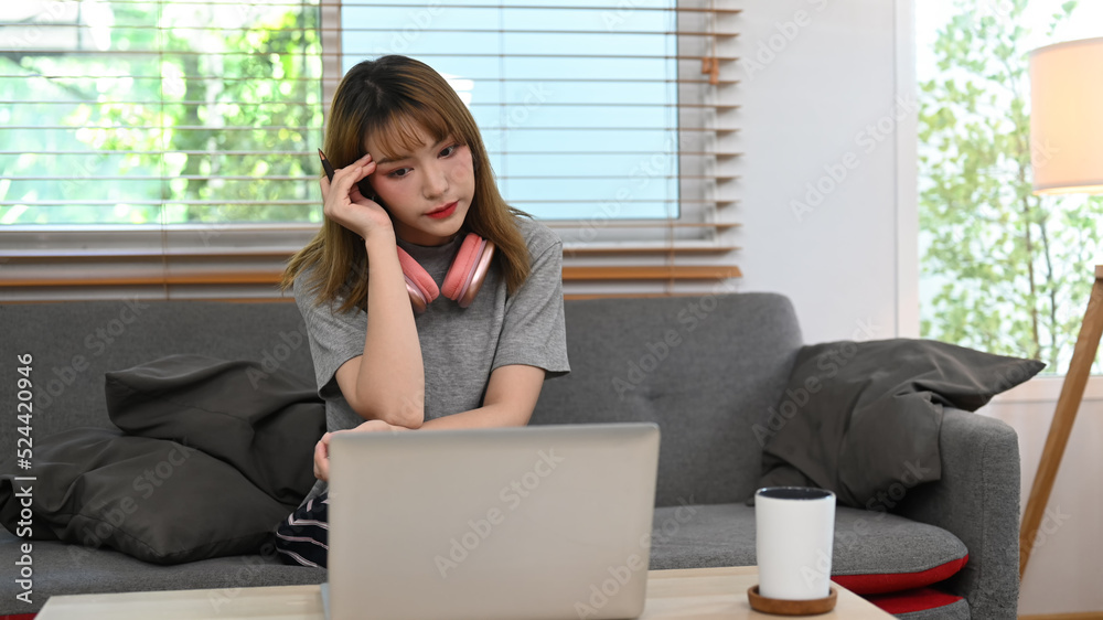 Serious young woman reading email, working online from home with laptop on couch Serious young woman reading email, working online from home with laptop on couch