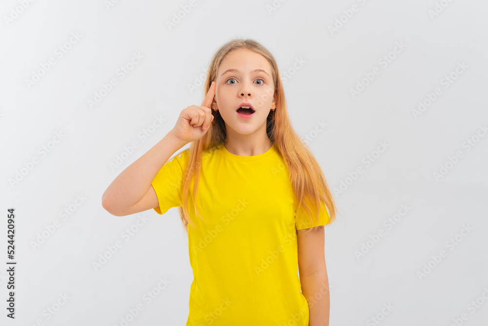 Amazed teen girl with blonde hair is thinking and holding a finger to his temple, making decision, standing over white background in yellow tshirt Amazed teen girl with blonde hair is thinking and holding a finger to his temple, making decision, standing over white background in yellow tshirt