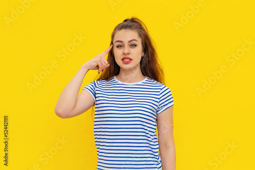 Portrait of thinking looking beautiful brunette girl 20s in casual white-blue striped t shirt, standing over yellow background