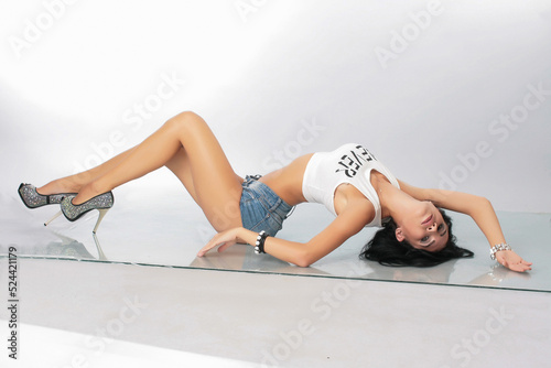 a pretty girl brunette stretching instructor, go-go, trainer, danser, posing in the studio on a white background in shorts and T-shirt