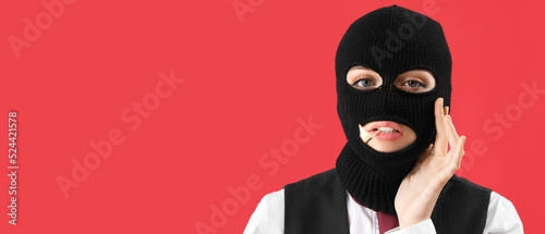 Portrait of young woman in balaclava and with burning match in mouth on red background with space for text photo