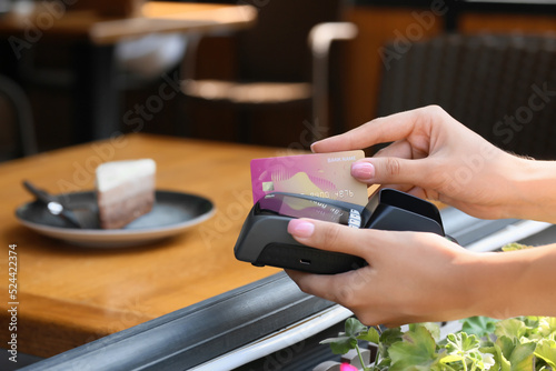 Woman paying for cake with credit card via payment terminal in cafe, closeup