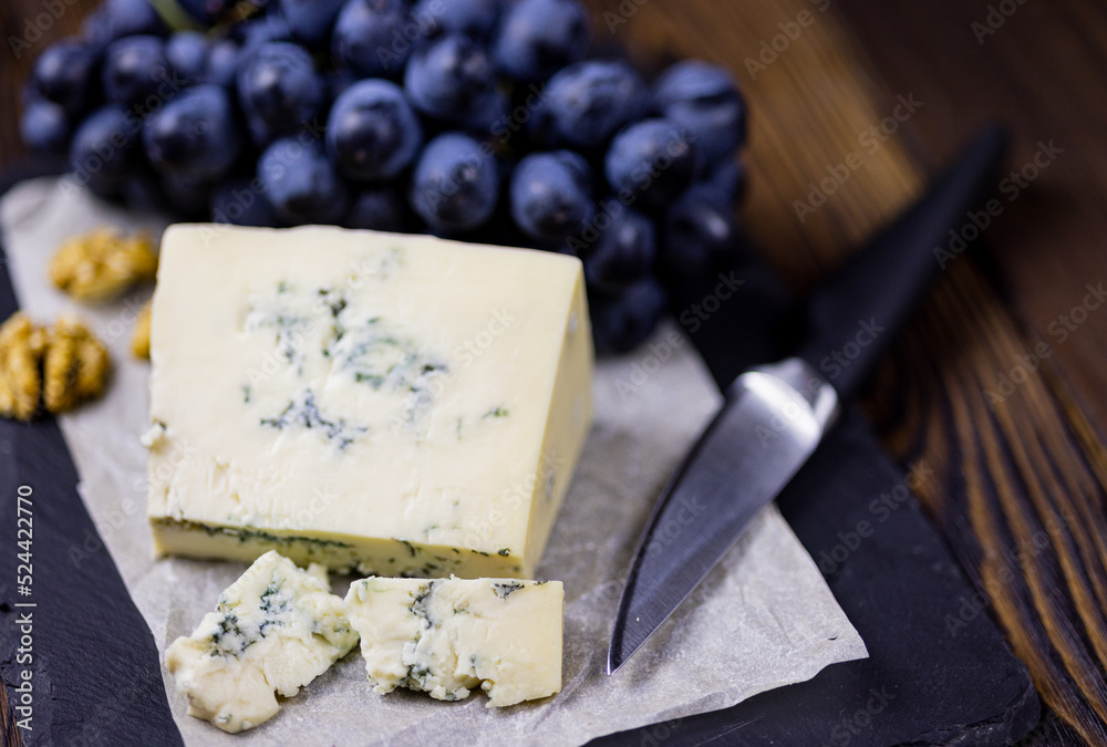 Tasty blue cheese served with grape and green on a wooden background. Dorblu cheese pieces