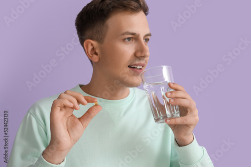 Young man with glass of water and vitamin on violet background