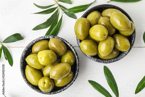 Composition with bowls of tasty green olives and leaves on light wooden background, closeup