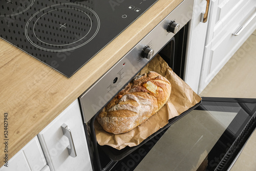 Oven with fresh bread on baking sheet in kitchen