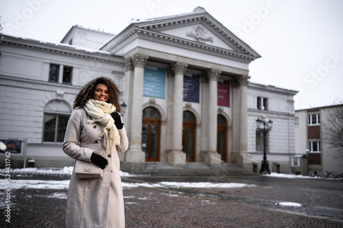 beautiful young black woman waiting in front of a theater for here friends in snow covered city photo
