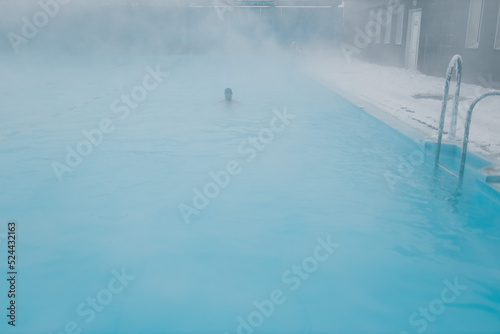 Fit swimmer male training swim in open winter swimming pool with fog. Geothermal outdoor spa health concept.