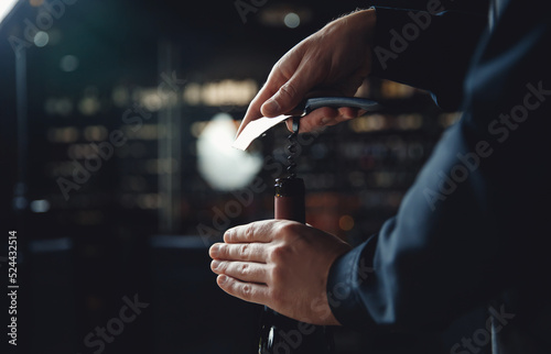 Sommelier opens cork of bottle of red wine with corkscrew photo