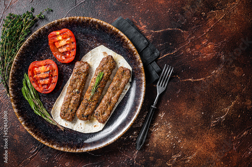 Grilled Urfa shish kebab on a plate with tomato. Dark background. top view. Copy space