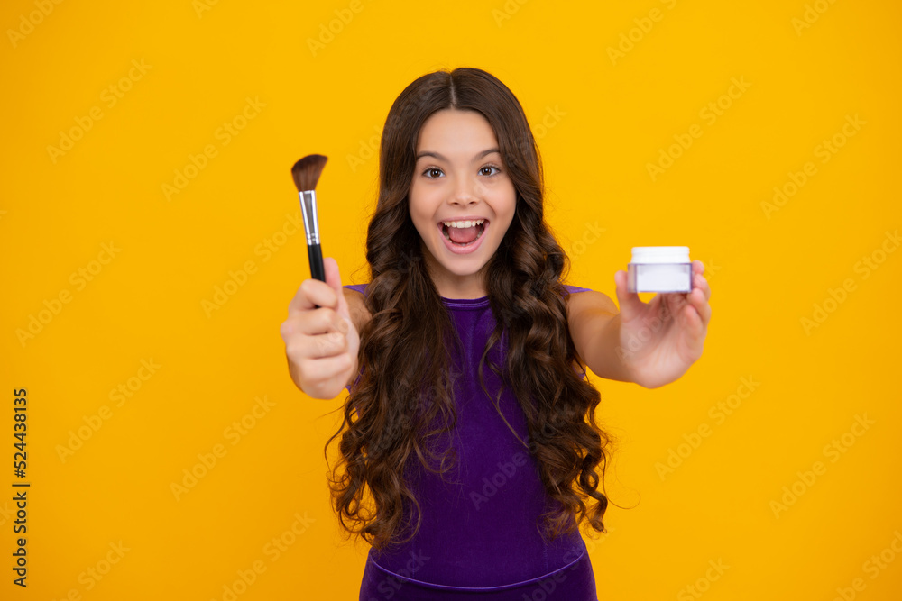 Beauty, make up and kids cosmetics. Teenage girl with brush applying blush to face isolated on yellow studio background. Happy girl face, positive and smiling emotions. Beauty, make up and kids cosmetics. Teenage girl with brush applying blush to face isolated on yellow studio background. Happy girl face, positive and smiling emotions.