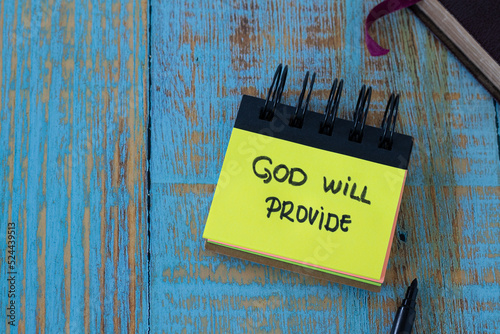 God will provide, a handwritten text note in a small notebook with a closed Holy Bible Book on a rustic wooden background. Top table view. Christian biblical concept. photo