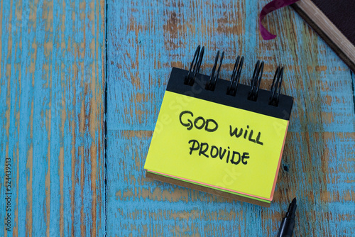 God will provide, a handwritten text note in a small notebook with a closed Holy Bible Book on a rustic wooden background. Top table view. Christian biblical concept.