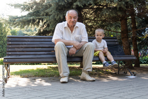 Grandfather and grandson are sitting on a bench in the park. An old man walks in the park with a little boy.