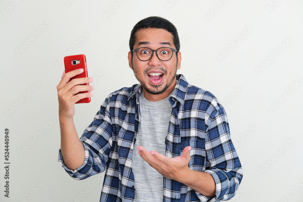 Young Asian man looking to camera showing wow expression while holding handphone Young Asian man looking to camera showing wow expression while holding handphone