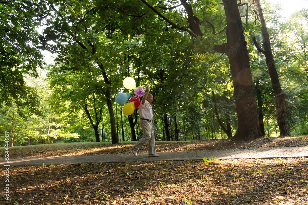 A lonely pensioner walks along the path in the park with balloons. An elderly man is having fun in the park among the trees. A lonely pensioner walks along the path in the park with balloons. An elderly man is having fun in the park among the trees.