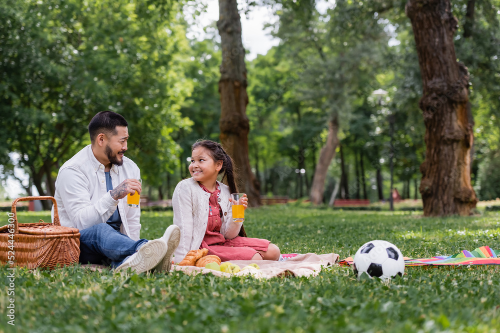 Asian family holding orange juice near food and football on grass in park. Asian family holding orange juice near food and football on grass in park.