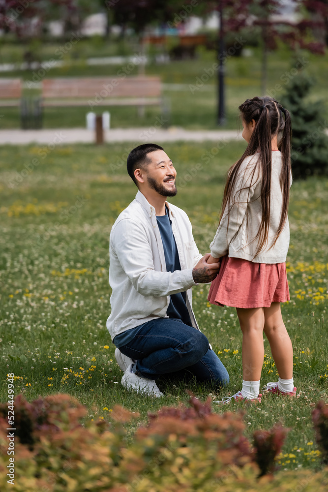 Happy asian parent holding hand of preteen daughter on meadow in park. Happy asian parent holding hand of preteen daughter on meadow in park.