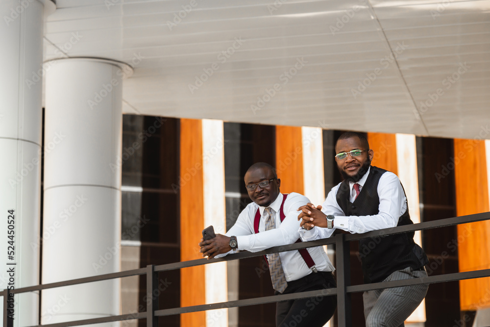 Portrait of two dark-skinned businessmen talking in the background of a modern building exterior. Friendly meeting outdoors