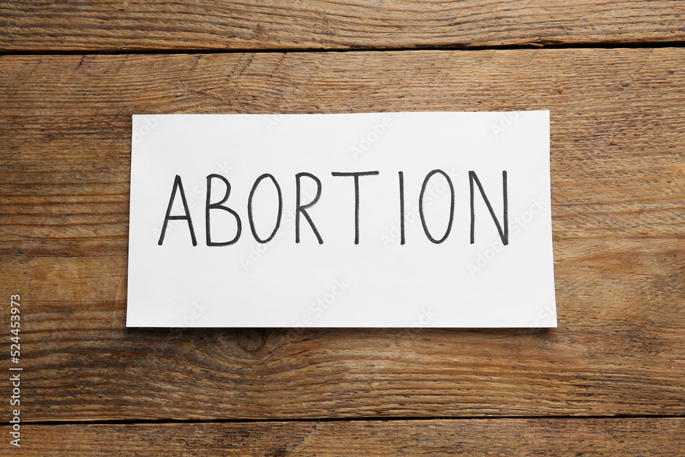 Paper note with word Abortion on wooden background, top view Paper note with word Abortion on wooden background, top view
